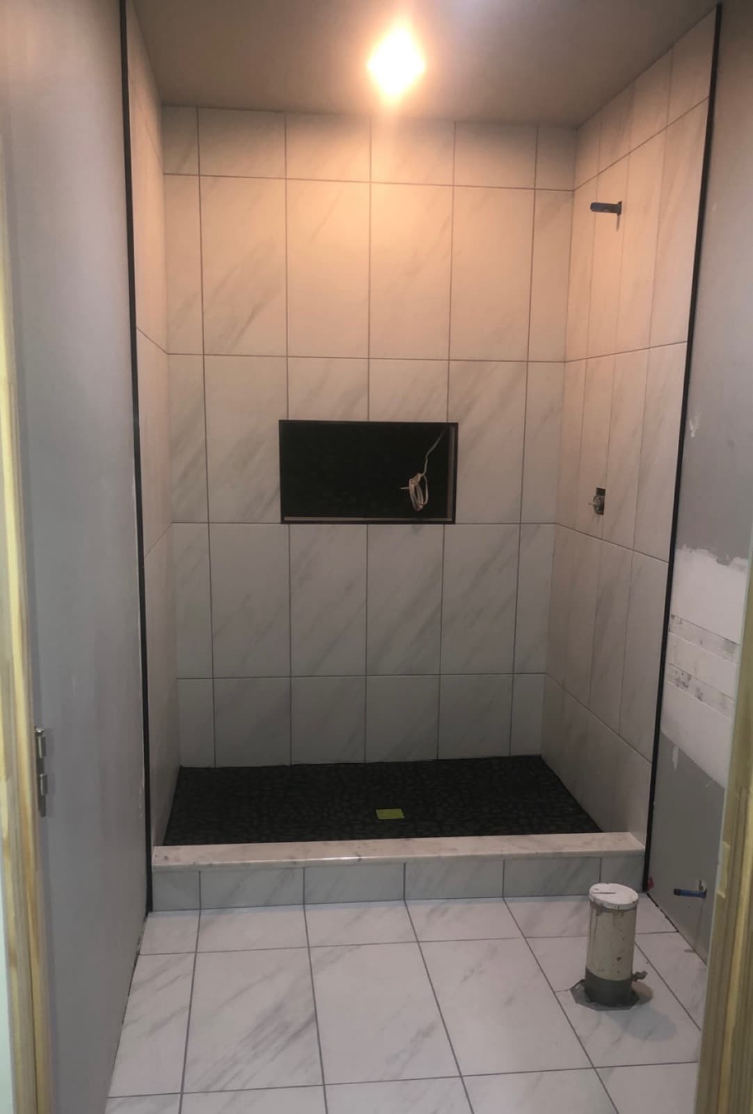 Walk-in shower with marble-look walls, pebble floor, and recessed niche