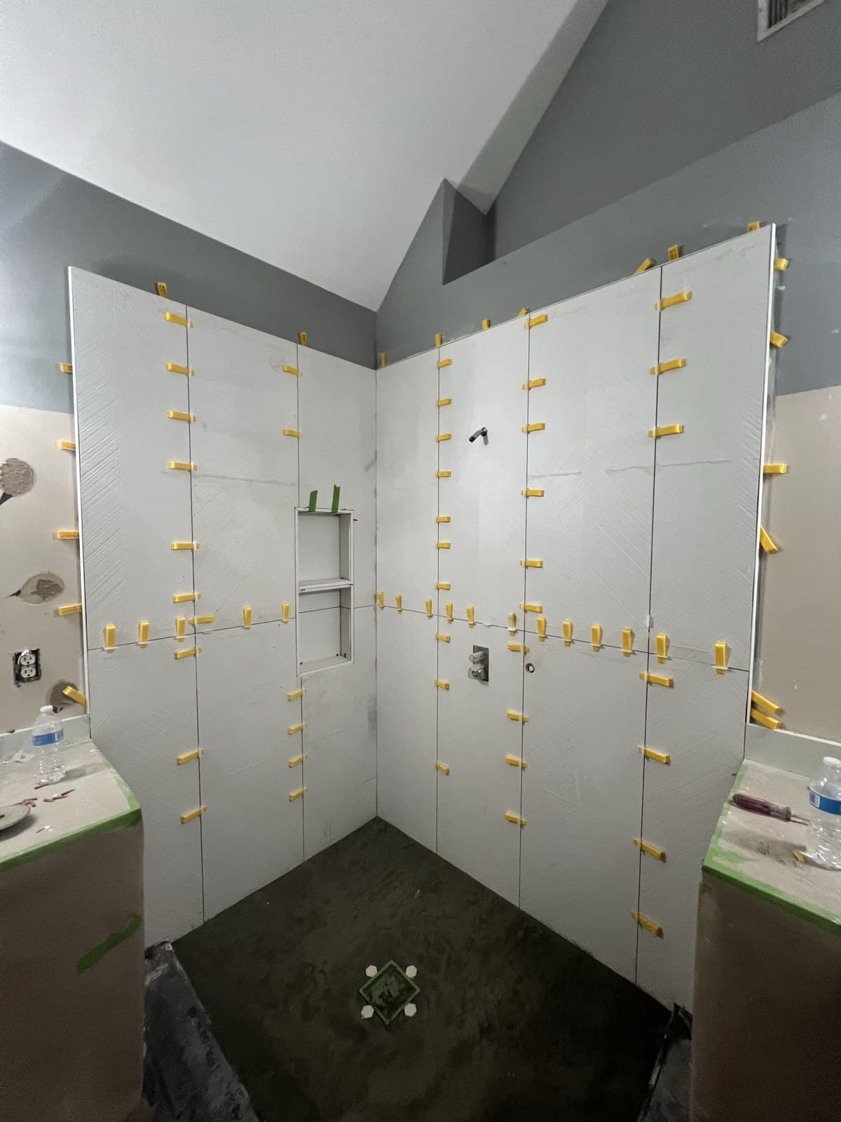 Large-format shower tile set with leveling clips during a bathroom remodel